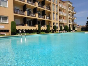 A swimming pool with clear blue water, surrounded by a multi-story building with balconies and a tiled exterior. - Apartments with swimming pool near the beach. Ref. Comte Empuries-46 (Empuriabrava)