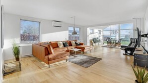 A spacious living room with a brown leather sofa, a dining area with a table and chairs, and large windows offering a view of the outdoors. - Gorgeous home in Sunds with kitchen (Sunds)