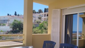 A balcony with a table set for two, two chairs, and a view of the surrounding buildings and greenery.