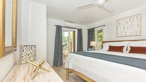 Ein Schlafzimmer mit einem Bett, einem Deckenventilator, einem Fenster mit Vorhängen und Blick ins Freie.