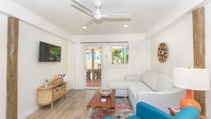 Ein Wohnzimmer mit weißem Sofa, blauem Sessel, Holztisch und Deckenventilator.