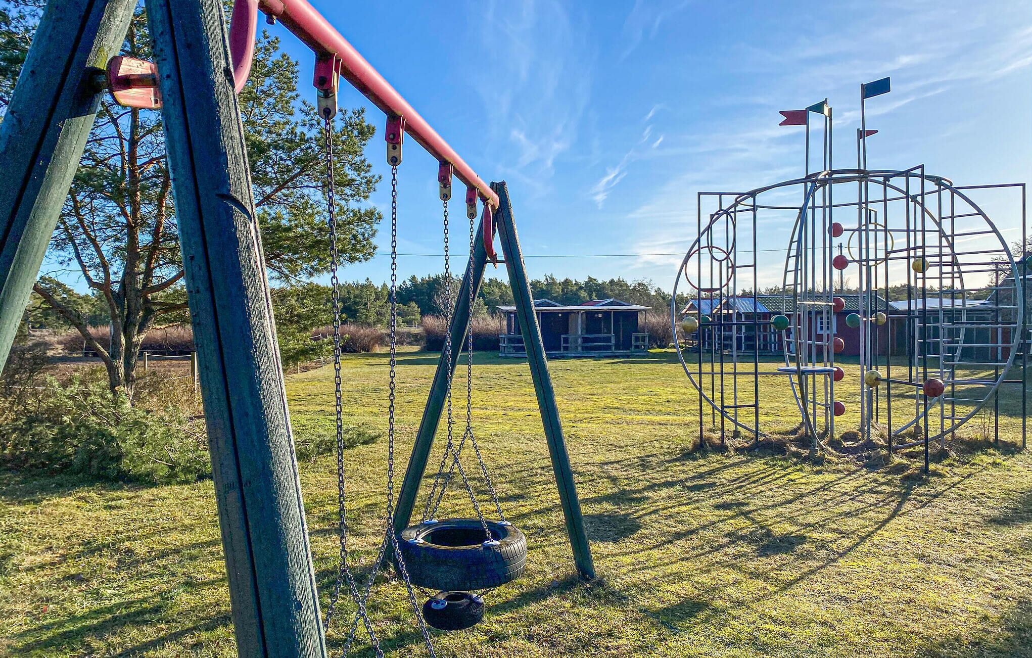 Une aire de jeux avec des balançoires, une balançoire en forme de pneu et une structure d’escalade en métal.