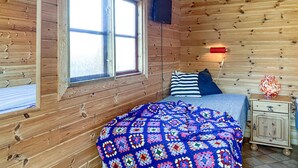 Una habitación acogedora con detalles de madera, una cama con colcha colorida, una mesita de noche con lámpara y una ventana con vistas.