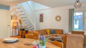 Een moderne woonkamer met een trap, een eethoek met een tafel, en een groot raam met uitzicht.