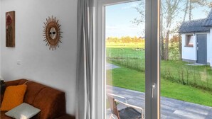 Een woonkamer met een bank, een zonachtige wanddecoratie en uitzicht op een grasveld door een schuifdeur.