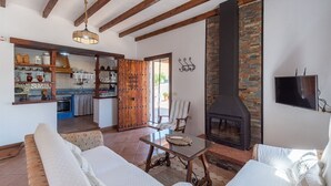 A spacious living area with a fireplace, a dining table, and a kitchen visible through an open door. - Casa La Era Villanueva de la Concepción by Ruralidays (Málaga)