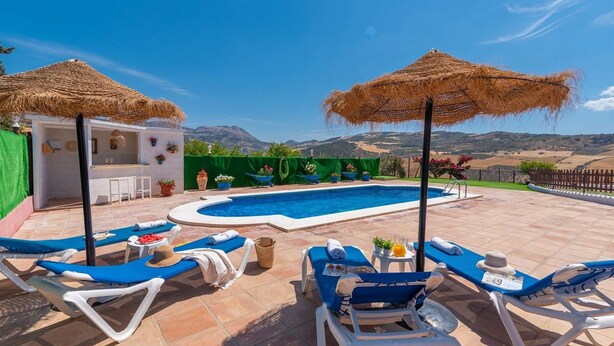 A pool area with lounge chairs and umbrellas, a bar, and a view of the mountains. - Casa La Era Villanueva de la Concepción by Ruralidays (Málaga)