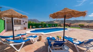 A pool area with lounge chairs and umbrellas, a bar, and a view of the mountains.