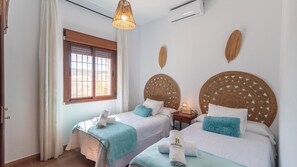 A hotel room with two beds, a window with curtains, a wall-mounted air conditioner, and decorative woven headboards. - Casa La Era Villanueva de la Concepción by Ruralidays (Málaga)