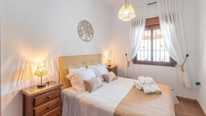 A neatly arranged bedroom with a bed, bedside lamps, a window with curtains, and a wall decoration. - Casa La Era Villanueva de la Concepción by Ruralidays (Málaga)