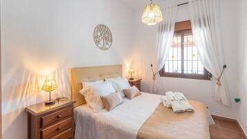 A neatly arranged bedroom with a bed, bedside lamps, a window with curtains, and a wall decoration.