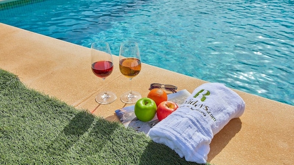 Ein Poolbereich mit Handtuch, zwei Weingläsern, einem Apfel, einer Orange und einer Zeitschrift.