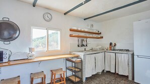 A compact kitchen with a stove, sink, and wooden counter. There are two stools and a window providing natural light. - Cortijo de Liche Arcos de la Frontera by Ruralidays (Cádiz)