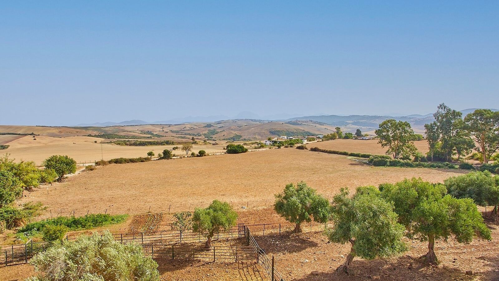 A rural landscape with fields, trees, and distant hills.