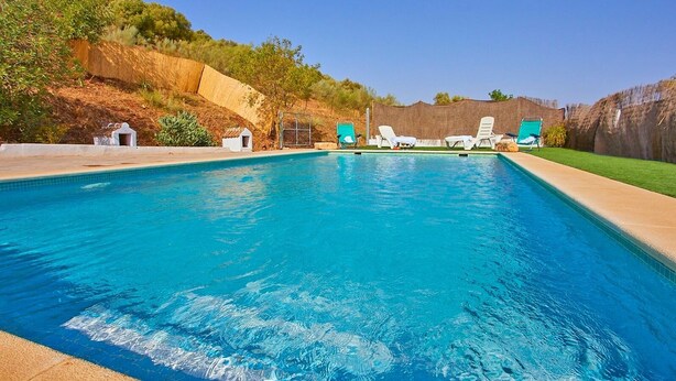 A rectangular swimming pool with clear blue water, surrounded by a grassy area and a wooden fence. - Cortijo de Liche Arcos de la Frontera by Ruralidays (Cádiz)