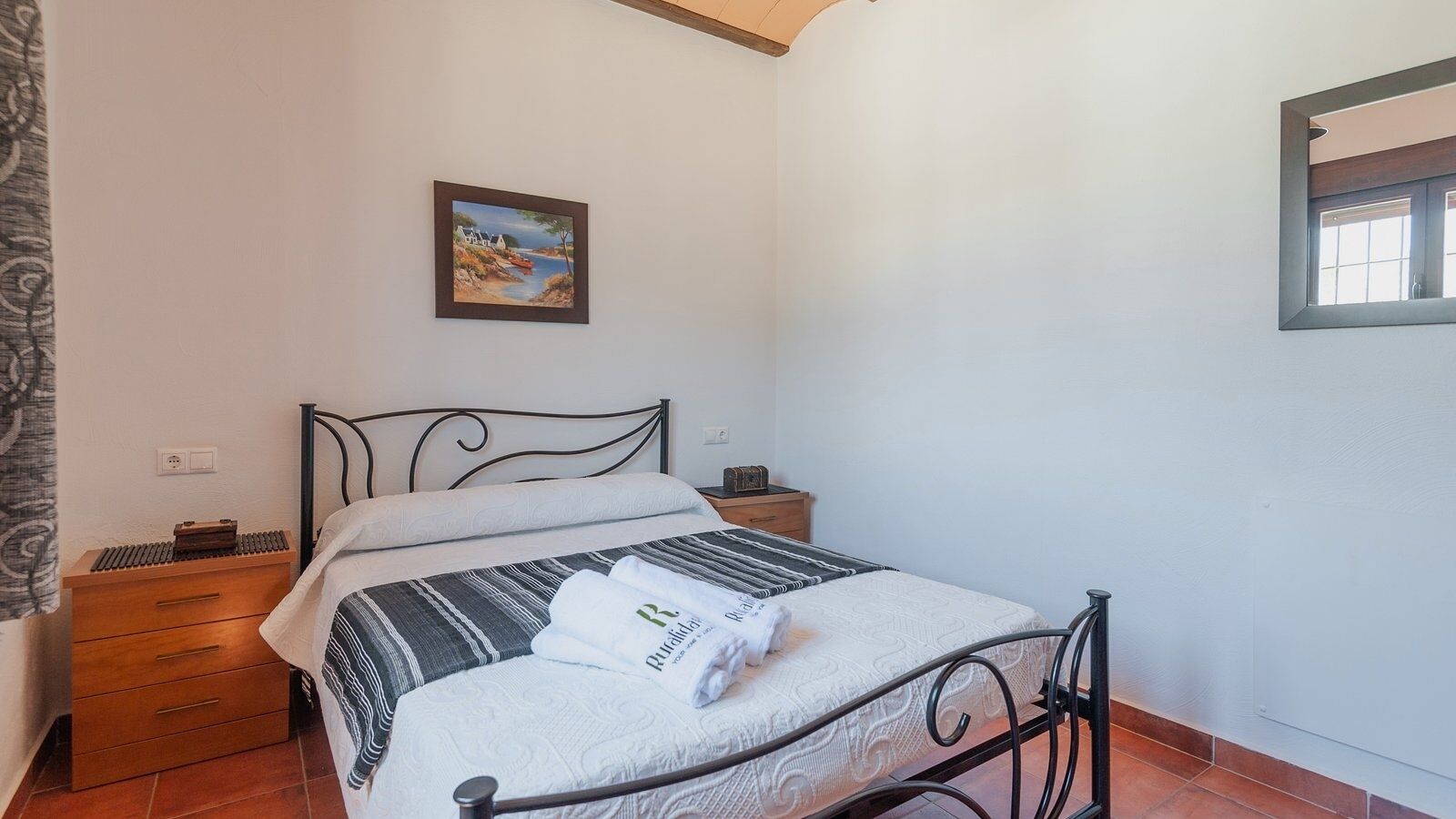 Une chambre à coucher avec un lit, des tables de chevet en bois, un tableau au mur et une fenêtre.