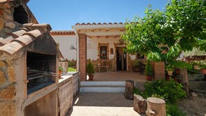 A stone-built outdoor kitchen area with a grill, potted plants, and a patio with a table and chairs.