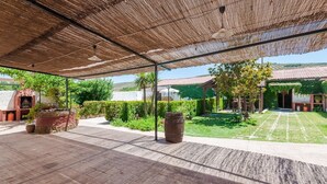 An outdoor patio area with a thatched roof, stone flooring, and potted plants.