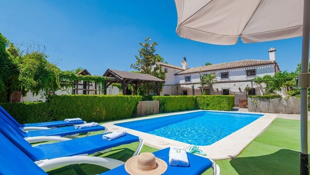A swimming pool with blue lounge chairs and a sun umbrella.
