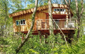 Ein hölzernes Baumhaus mit Balkon, umgeben von dichtem Wald.