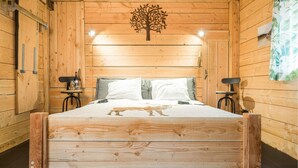 Una habitación de madera con una cama, dos mesitas de noche y una lámpara fijada a la pared.