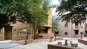 An outdoor courtyard with a stone bench, a trash can, and a mailbox.
