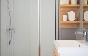 Bathroom features a glass shower enclosure and a white sink, along with a shelf for toiletries.