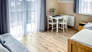 A bedroom with a bed, a small desk with a chair, a radiator, and a window with curtains. - Awesome apartment in Karwia (Karwia)