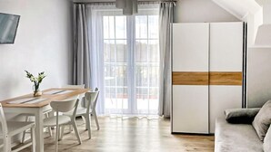 A modern, well-lit room with a wooden dining table, white chairs, a grey sofa, and a large window with sheer curtains. - Awesome apartment in Karwia (Karwia)