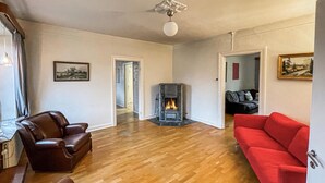 A living room with a fireplace, leather chairs, a red sofa, wooden flooring, and a painting on the wall.