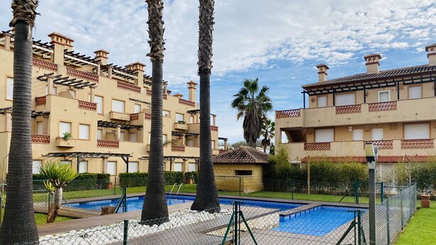 A residential building with multiple balconies, a swimming pool, and palm trees.