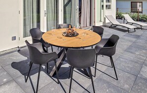 Et rundt træbord med seks sorte stole, en flaske og vinglas på en terrasse med fliset gulv.