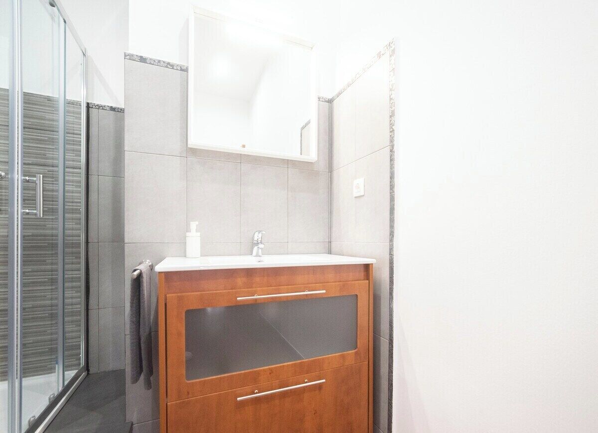 Un baño con cabina de ducha de vidrio, tocador de madera con espejo y lavabo blanco.
