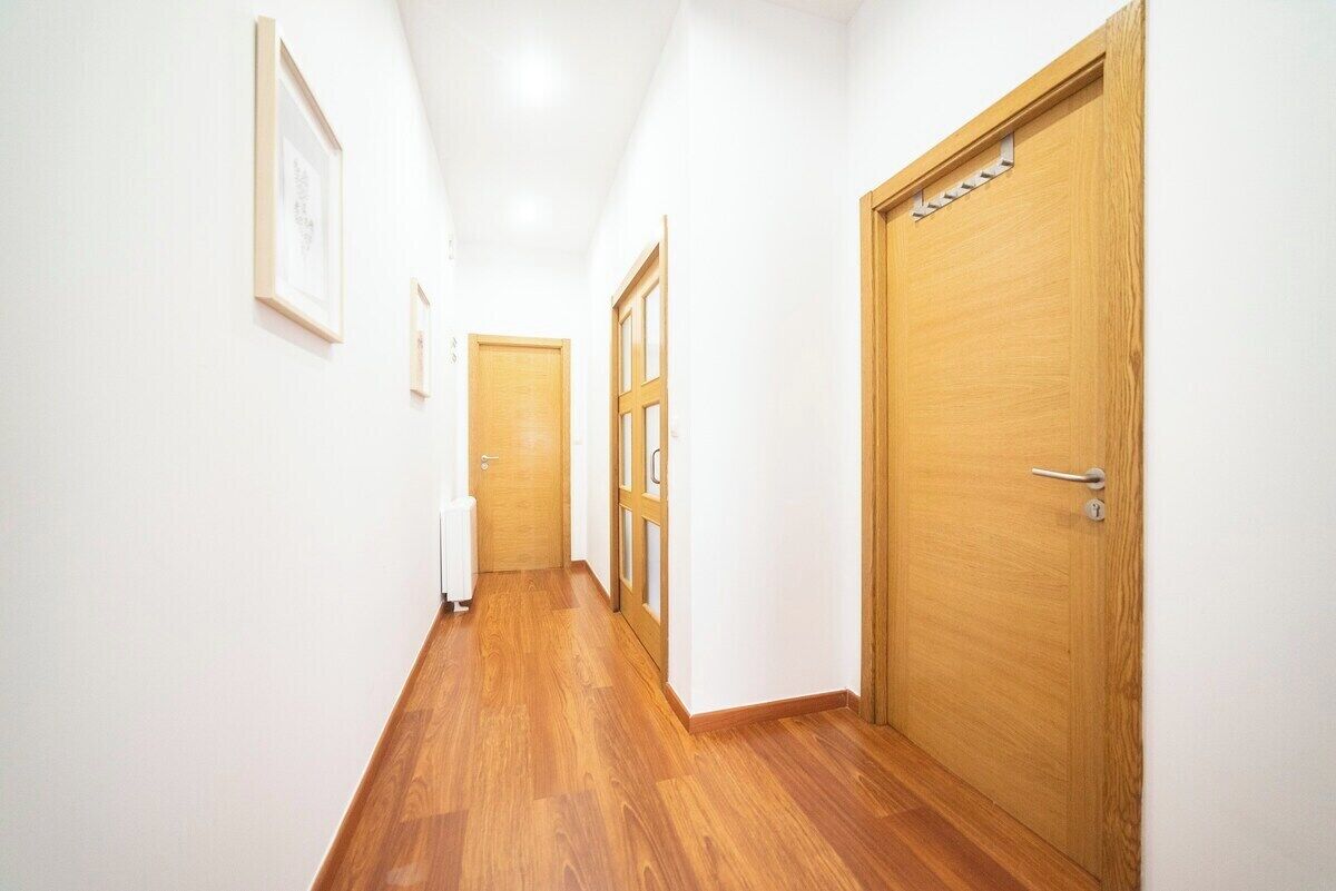 Un pasillo con suelo de madera y paredes blancas que conduce a una puerta con picaporte.