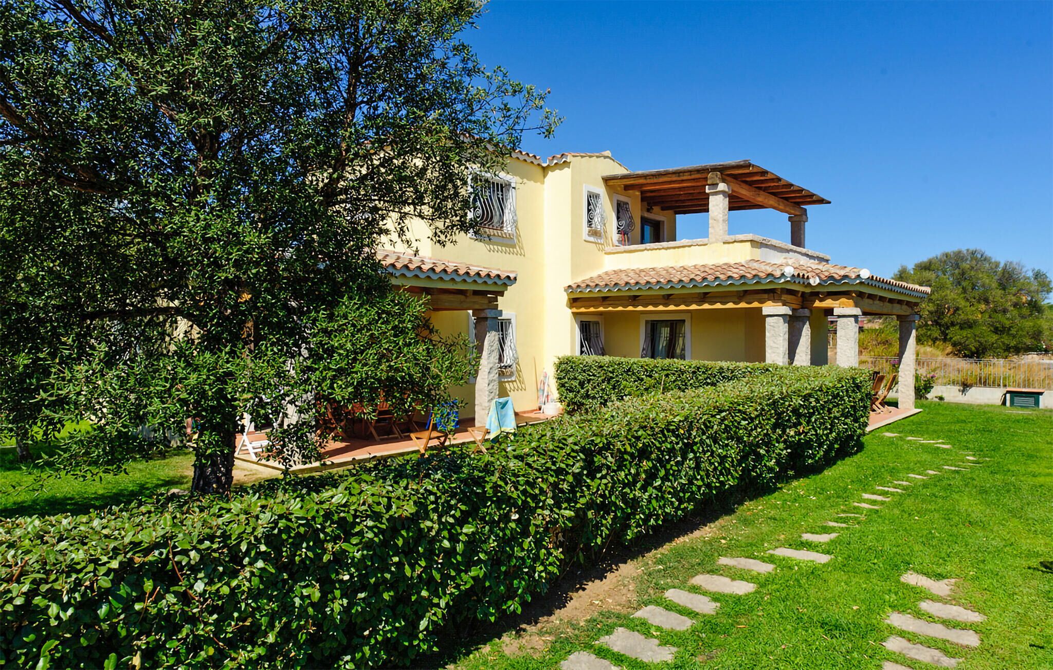 Una casa a due piani con tetto in tegole, un portico coperto e un giardino curato con siepe e pietre per il cammino.