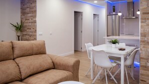 Een moderne woonkamer met een bruine bank, een witte eettafel met stoelen, en een keuken met een roestvrijstalen afzuigkap.