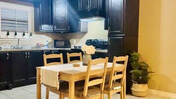 A kitchen with dark cabinets, a wooden table, and chairs. There is a potted plant and a vase with flowers on the table.
