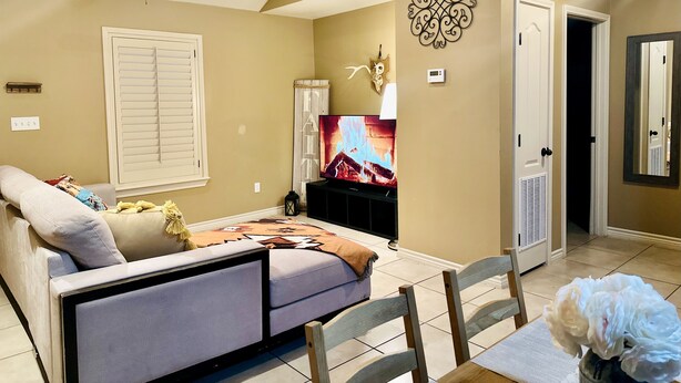 Un salon comprenant un canapé, un téléviseur, un ventilateur de plafond, des œuvres d’art décoratives au mur et une porte donnant sur une autre pièce.