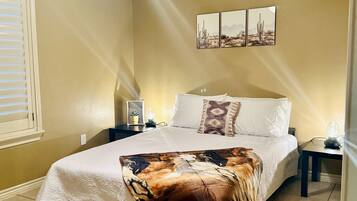 A bedroom with a bed, a ceiling fan, a nightstand, a wall-mounted picture, and a window with blinds.