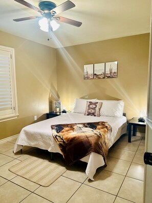 A bedroom with a bed, a ceiling fan, a nightstand, a wall-mounted picture, and a window with blinds. - Western Style - 2 bed/1 bath - RATED 5 STARS (Eagle Pass)