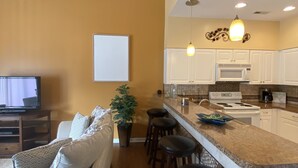 A modern kitchen with white cabinets, a microwave, and a stove. There is a bar area with stools and a potted plant.
