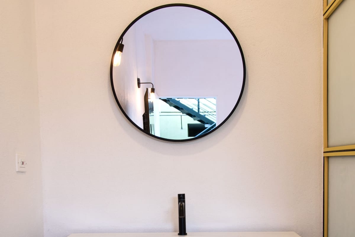 A bathroom with a round mirror, a white sink, and two towels hanging on a rack.