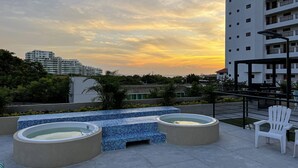 Terraço no telhado com hidromassagem, área de estar e vista para o horizonte urbano ao pôr do sol.