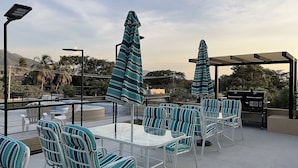 Terraço no telhado com cadeiras e mesas listradas, uma churrasqueira e guarda-sóis.