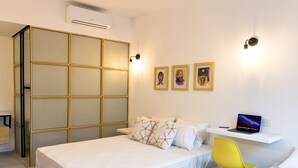 Quarto moderno com uma cama, uma escrivaninha com um laptop, uma cadeira amarela e um guarda-roupa com porta de vidro.