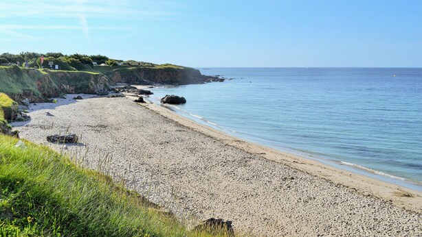 En strand med en stenig kustlinje, gräsbevuxna områden och fri utsikt över havet.