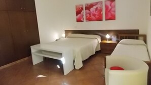 Une chambre d’hôtel comprenant un lit, une chaise, une table de chevet et un mur orné de trois tableaux représentant des motifs floraux rouges.