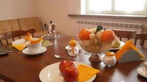 Une table à manger avec des assiettes remplies de nourriture, un panier de fruits et une cafetière.