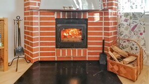 Een metselwerk open haard met vuur, een metalen draaispit en een mand hout.