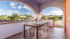 Ein Balkon mit Tisch und Stühlen, einer Weinflasche und einem Glas. Der Balkon bietet Blick auf Häuser und Bäume.